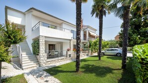 Una casa moderna de dos pisos con fachada de piedra, un balcón y un coche estacionado en la entrada.