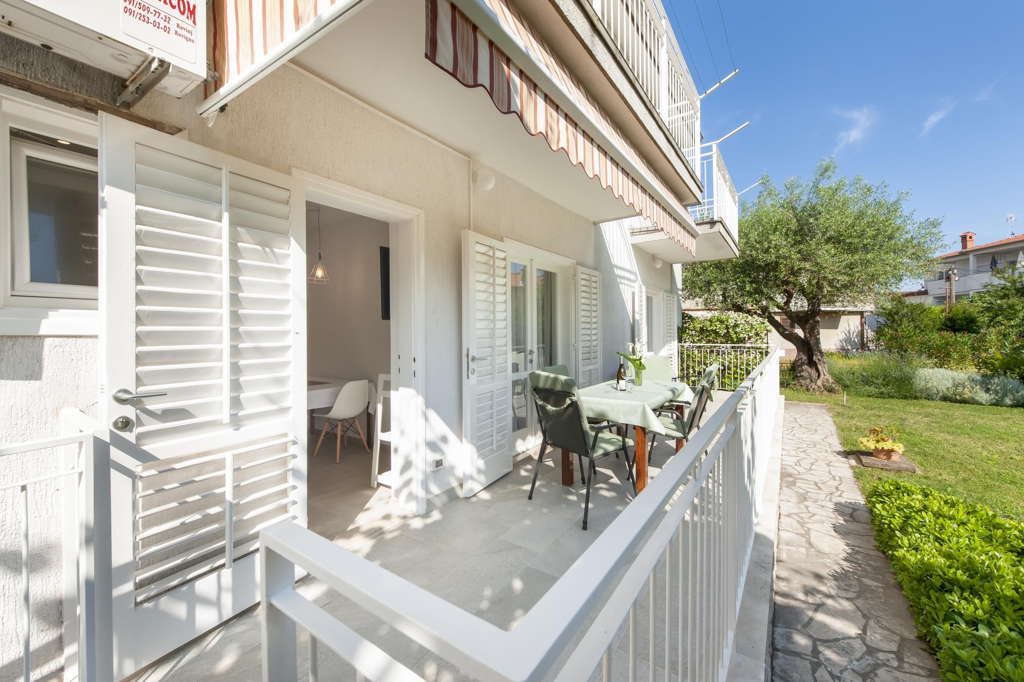 A white building with a balcony, a table with chairs, and a small garden area.
