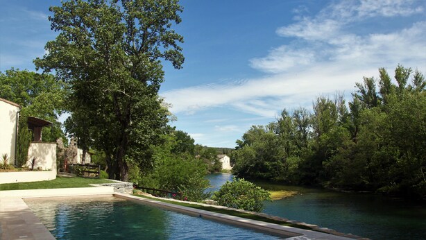 A swimming pool with a stone border, surrounded by lush greenery and a clear blue sky.