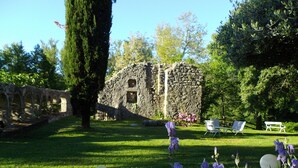 A garden with a stone structure, green grass, and purple flowers.
