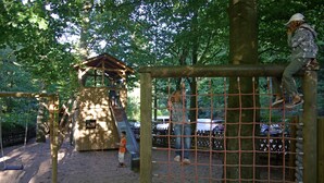 A playground with a wooden play structure, a slide, and a netted climbing area. - Naturfreundehaus Rahnenhof (Carlsberg)