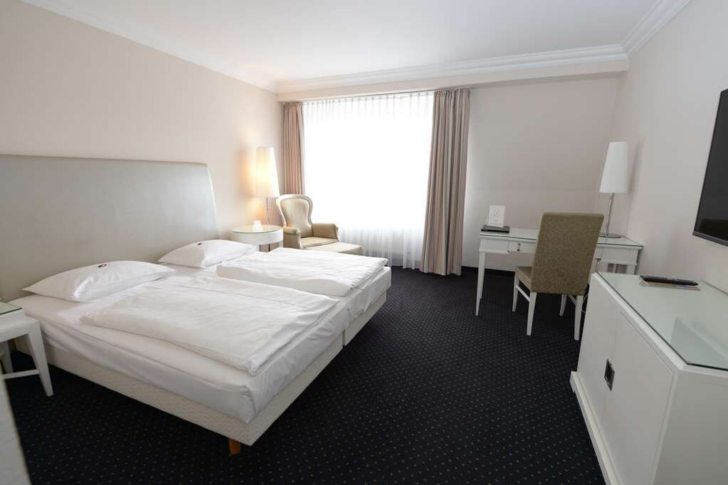 A hotel room with a large bed, a desk, a chair, and a TV.
