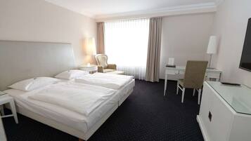 A hotel room with a large bed, a desk, a chair, and a TV.