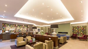 A hotel lobby with a reception desk, seating area, bar, and artwork on the walls.