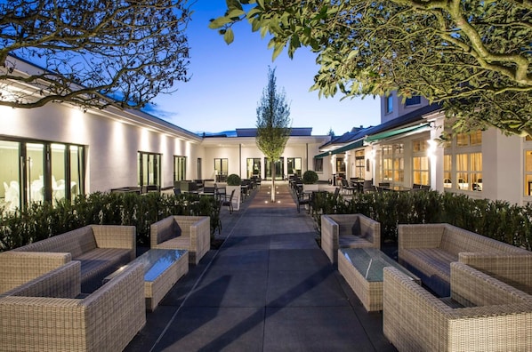 A courtyard with outdoor seating, a central pathway, and a building with large windows and doors.