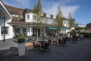 An outdoor café area with tables and chairs, surrounded by buildings with a mix of architectural styles.