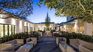 A courtyard with outdoor seating, a central pathway, and a building with large windows and doors.