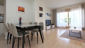 A modern living room with a dining area, a flat-screen TV, and a large window with sheer curtains. - Apartments Makado (Rovinj)