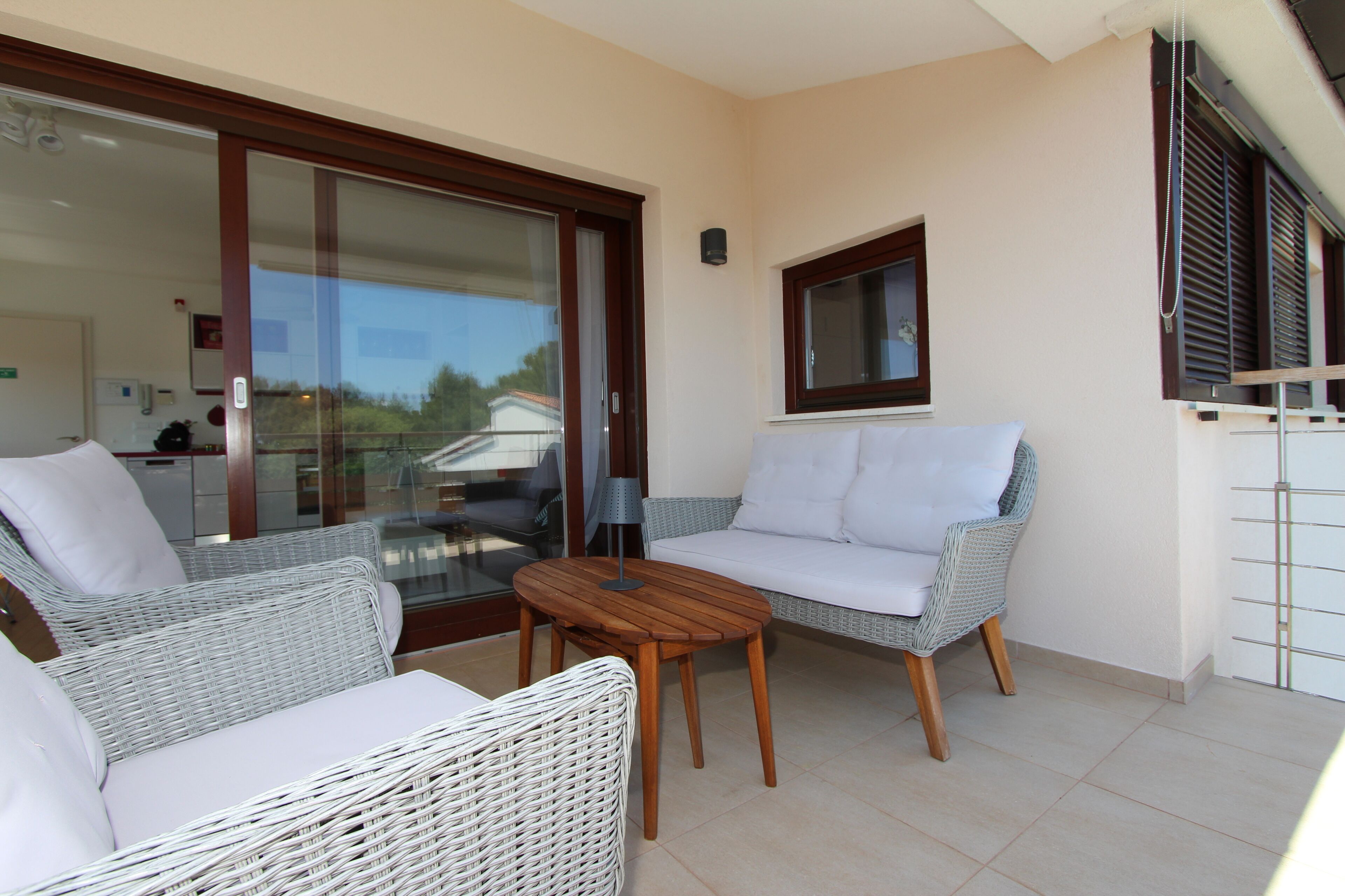 A balcony with wicker furniture, a wooden table, and a view of the outside.