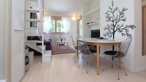 A modern living room with a dining area, a white sofa, a small table, and a decorative tree wall art. - Apartments Makado (Rovinj)