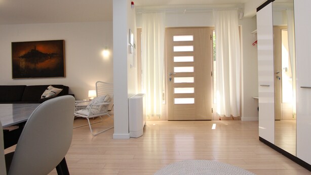 A modern living room with a sofa, a dining table, and a white chair. There is a painting on the wall and a door with a window. - Apartments Makado (Rovinj)