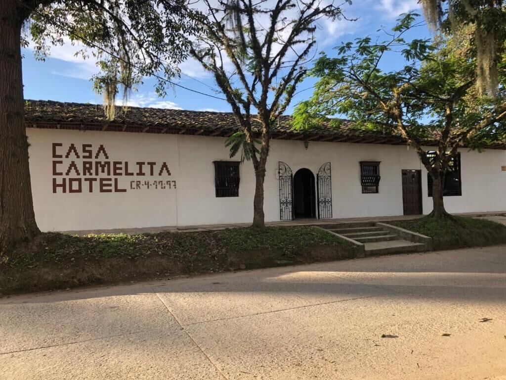 Un bâtiment blanc avec une enseigne indiquant « HÔTEL CASA CARMELITA » et une entrée avec un portail.