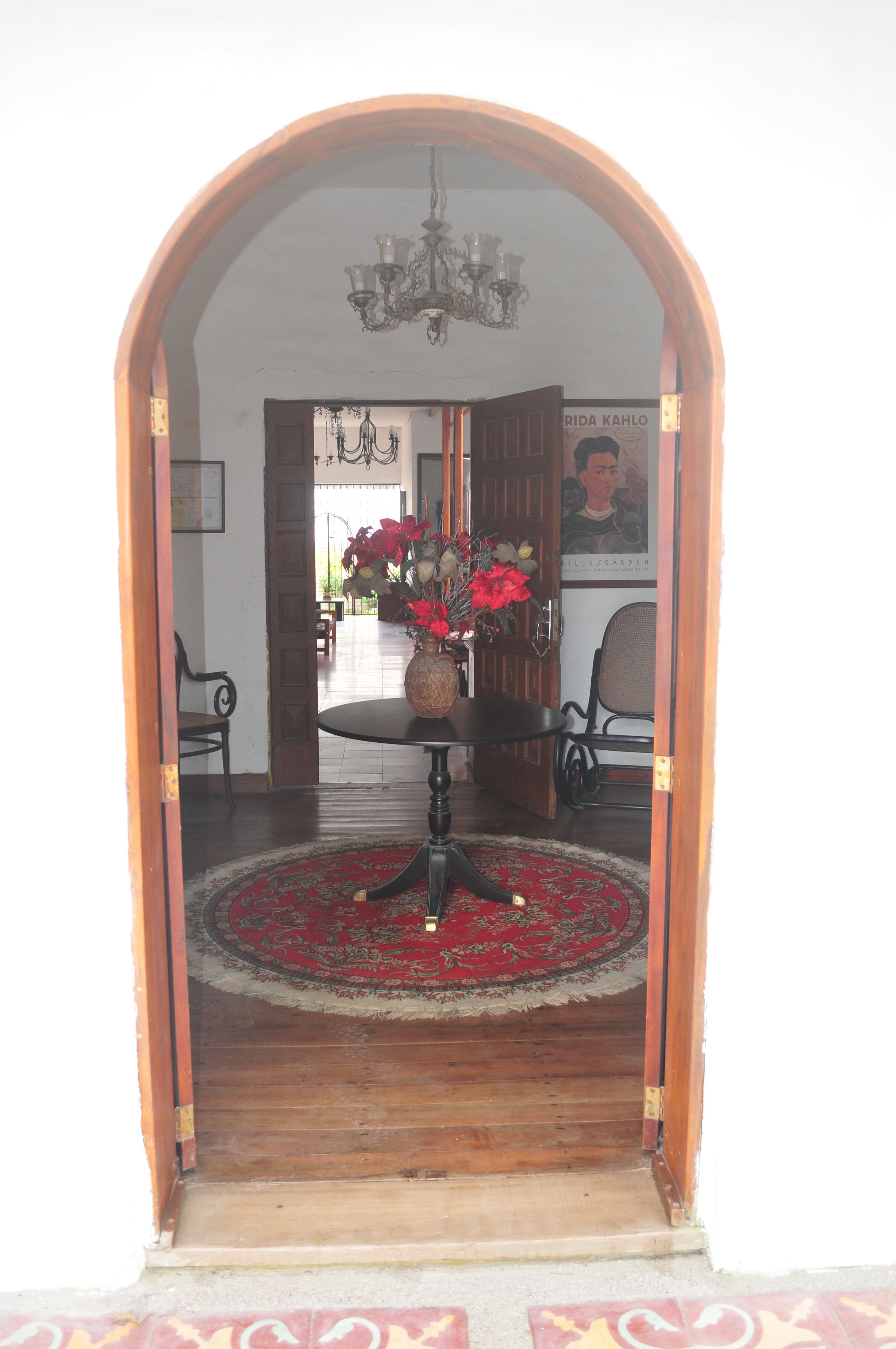 An arched doorway leading to a dining area with a table and chairs, a chandelier, and a poster on the wall.