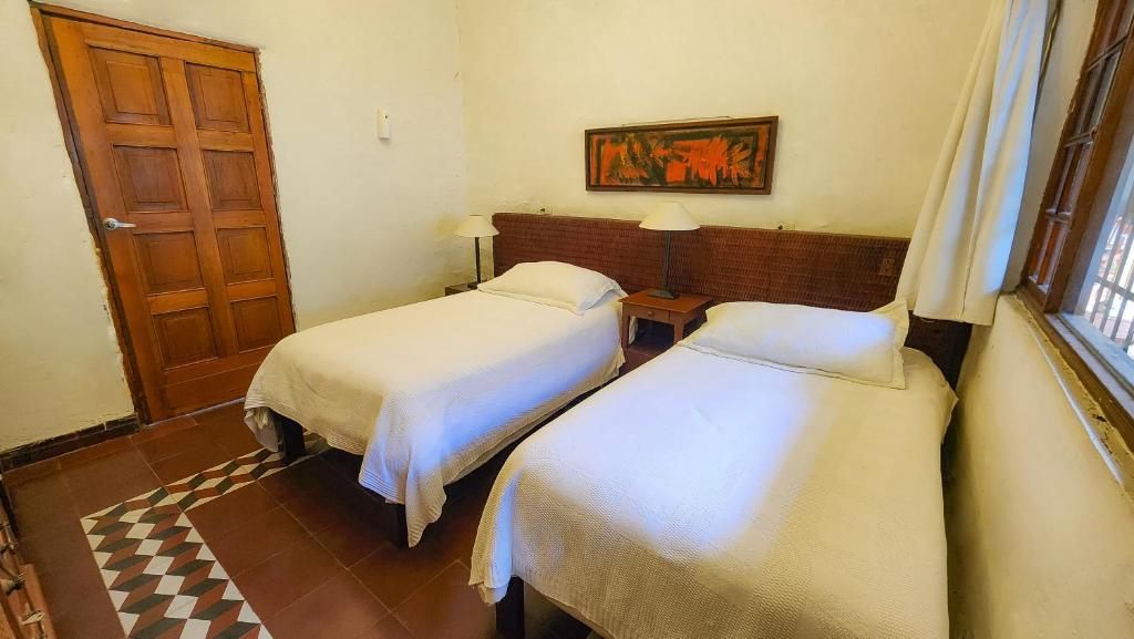 Una habitación con dos camas, una puerta de madera, un cuadro en la pared y un suelo estampado.