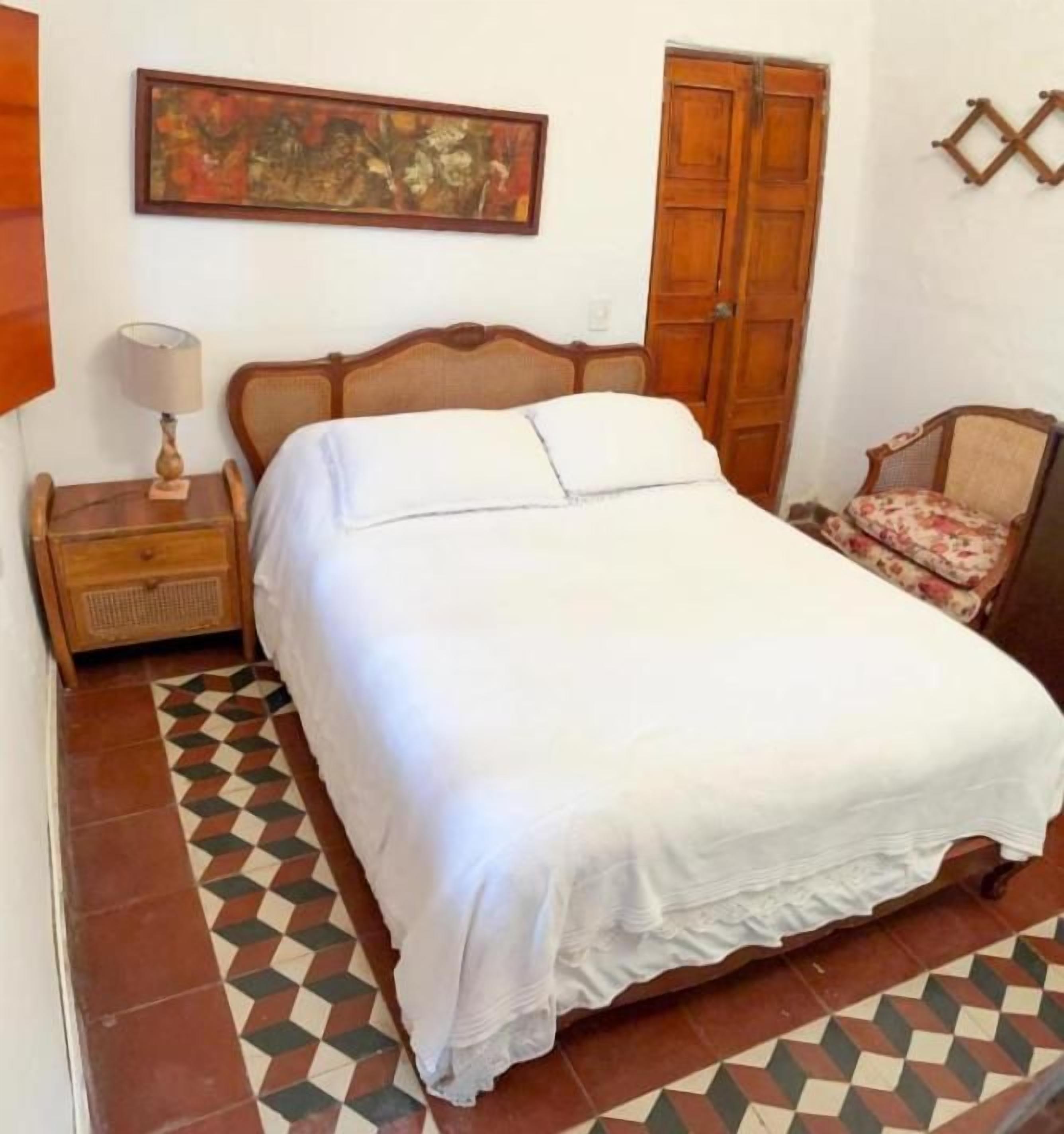 Une chambre à coucher comprenant un lit, une table de chevet, une chaise, une armoire et un tableau accroché au mur.