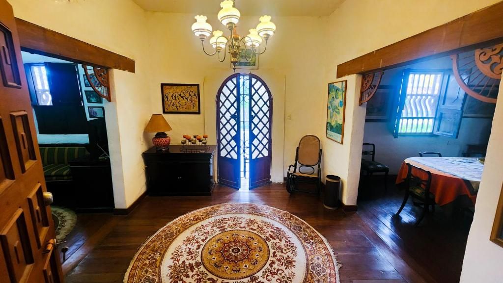 A room with a wooden floor, a patterned rug, a chandelier, a door with a decorative glass design, and a dining area with a table and chairs.