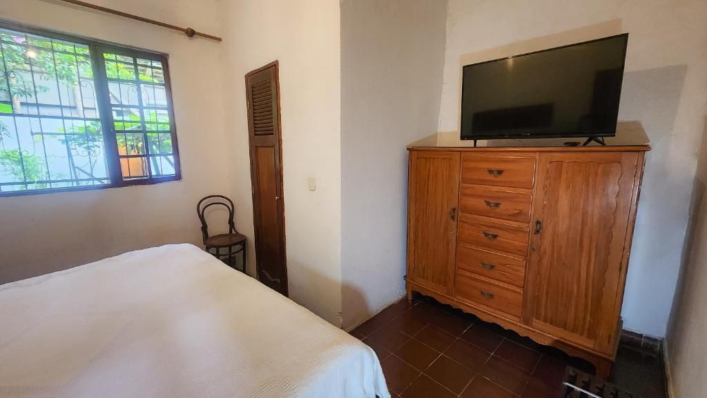 Un dormitori amb llit, armari de fusta, televisió a la part superior i finestra amb reixes.