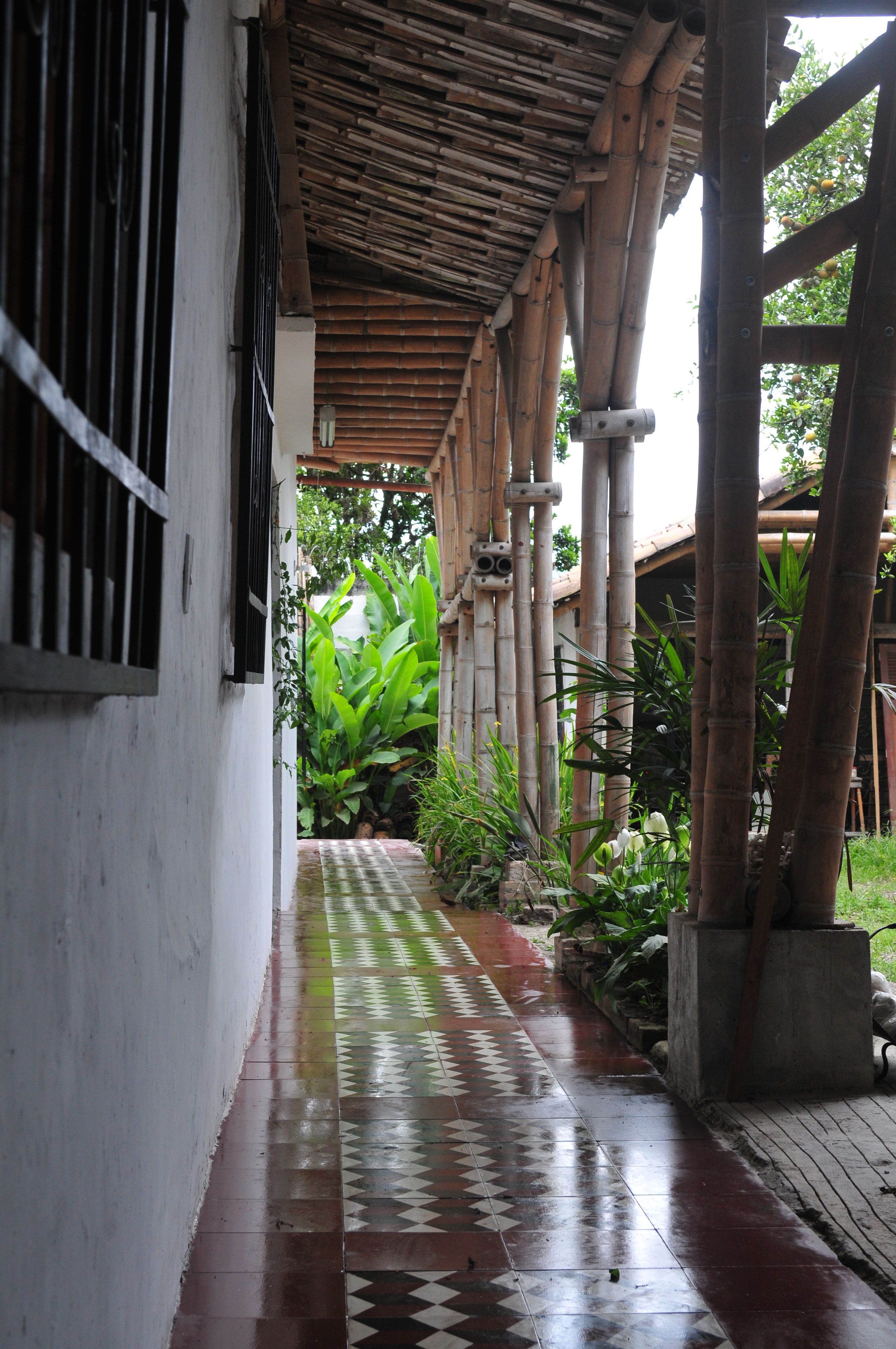 A corridor with a tiled floor, bamboo columns, and a covered area with a roof.