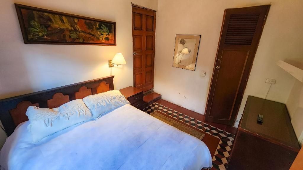A hotel room with a bed, a wooden wardrobe, a door, and a painting on the wall.