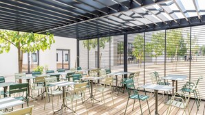 Une terrasse extérieure avec des tables et des chaises, une terrasse en bois et une pergola en métal.