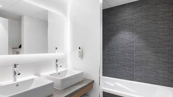 A modern bathroom with two sinks, a large mirror, and a bathtub.