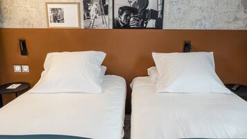 A hotel room with two beds, white linens, a brown headboard, a wall-mounted TV, and a framed photo above the beds.