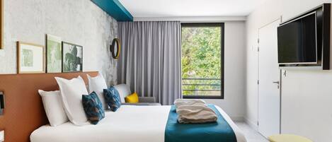 Habitación de hotel moderna con una cama grande, televisión, una mesita y ventana con vistas a zonas verdes.