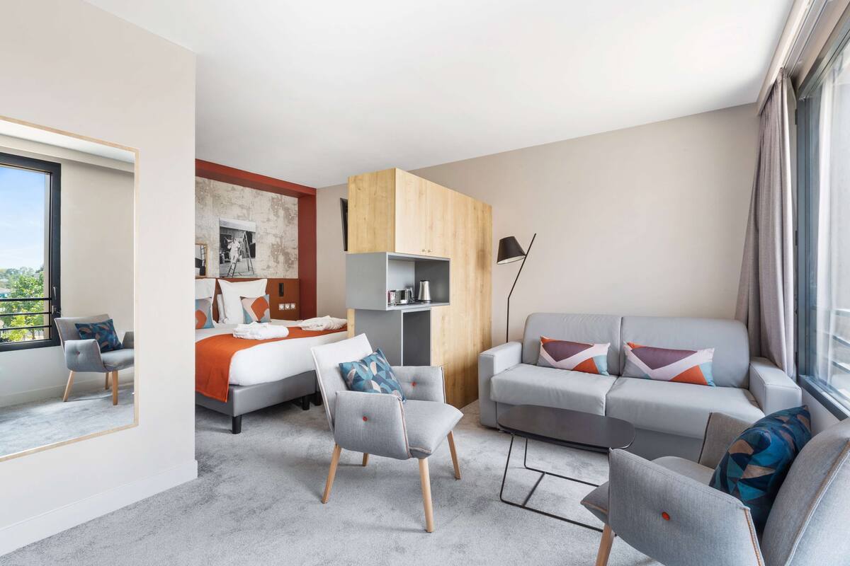 A modern hotel room with a bed, two sofas, a chair, and a desk.