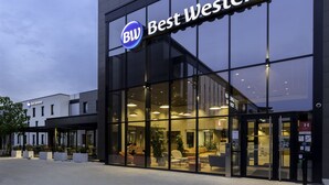 Un hôtel Best Western doté d’une façade moderne en verre, d’un espace extérieur aménagé et dont le mobilier intérieur est visible de l’extérieur.