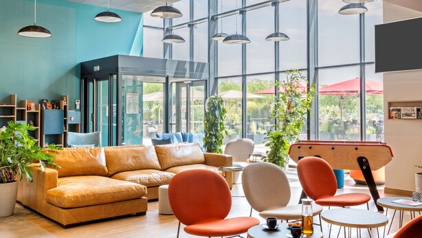 Un espace de détente moderne avec un canapé en cuir, des fauteuils orange et une table de billard.