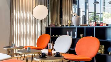 Ein modernes Interieur mit runden Tischen, orangefarbenen Stühlen, einer großen Vase und einem Regal mit diversen Gegenständen.