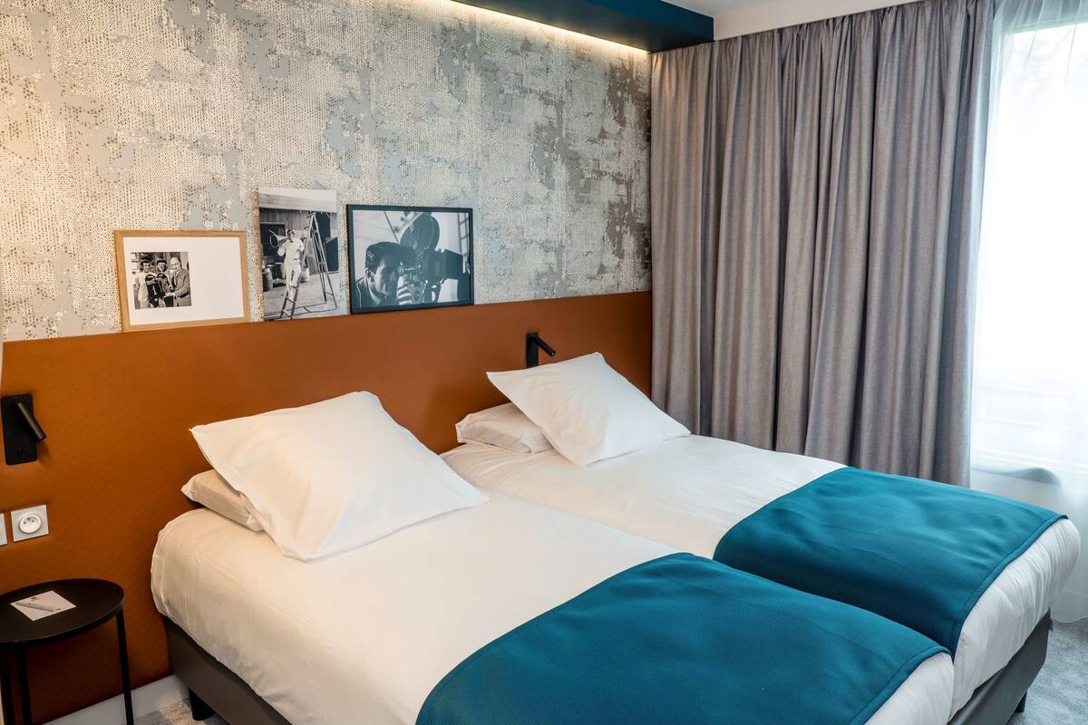 A double bed with white and teal bedding, a headboard, and a wall with two framed photographs.