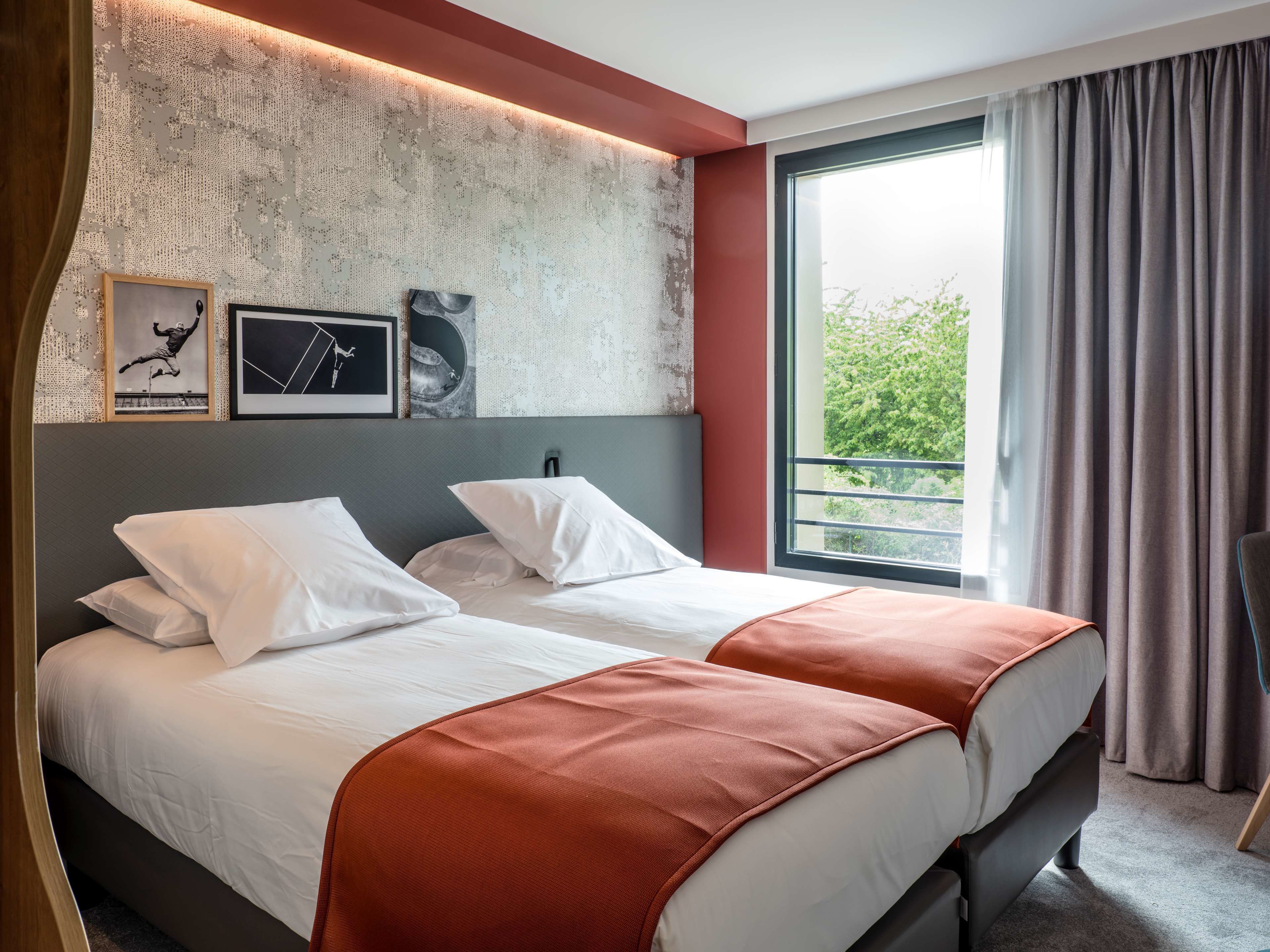 A hotel room with two beds, a large window with curtains, and artwork on the wall.