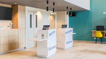 A reception area with two white reception desks labeled "Bienvenue" and a teal wall with a dotted pattern.