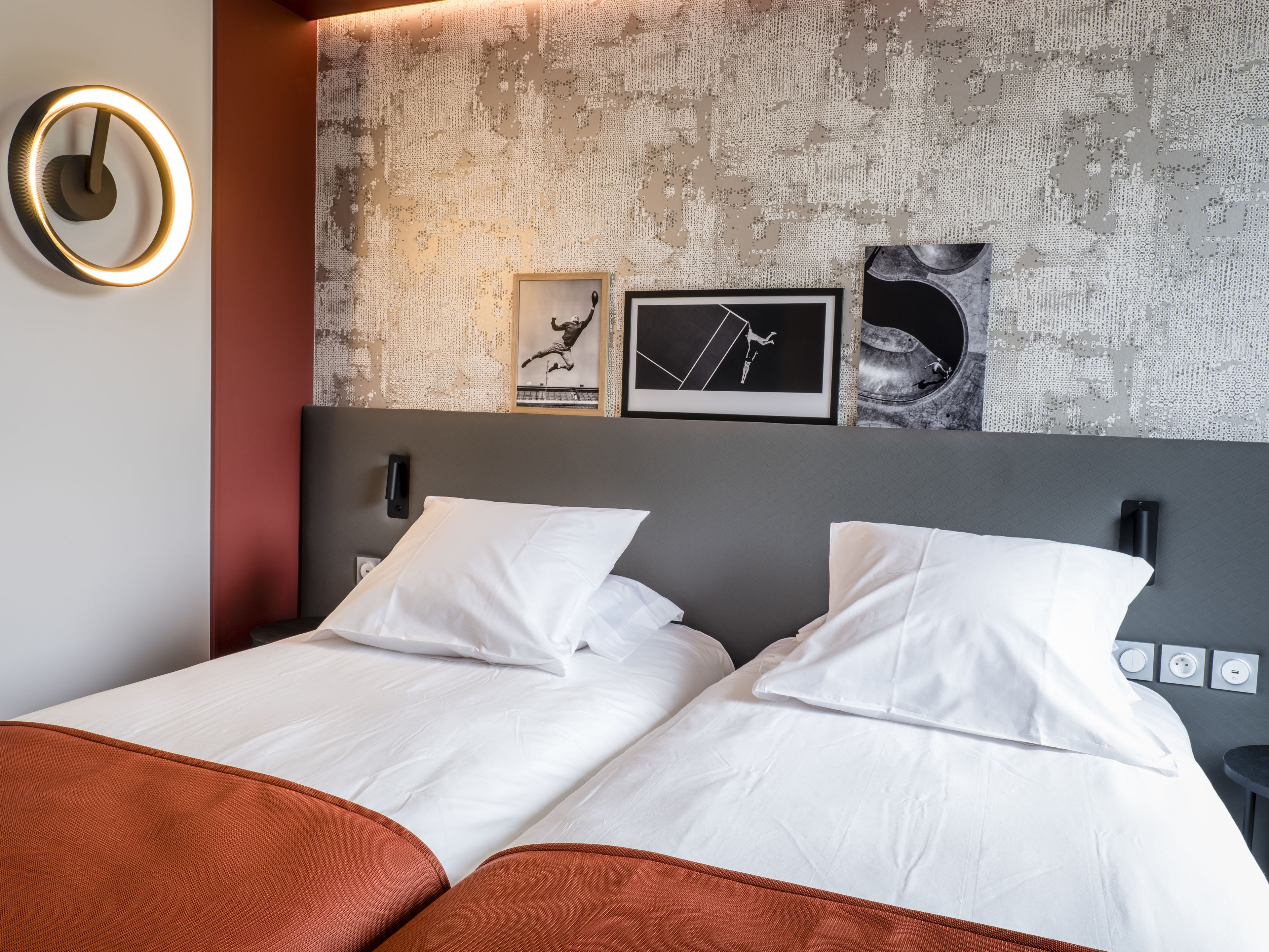 A modern hotel room with a large bed, two pillows, a headboard with artwork, and a wall-mounted light fixture.