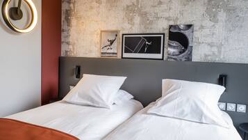A modern hotel room with a large bed, two pillows, a headboard with artwork, and a wall-mounted light fixture.