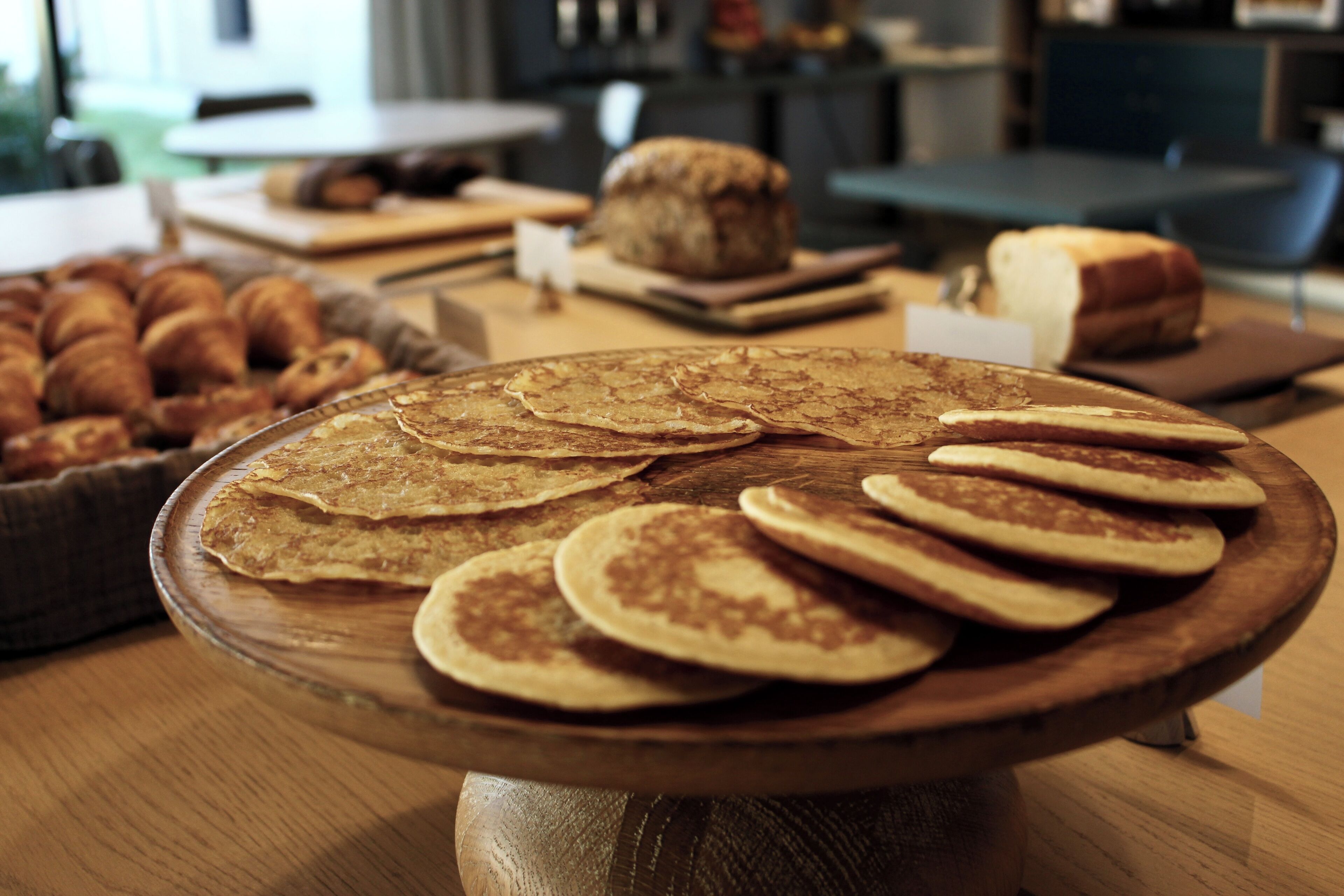 Un plateau de service en bois avec des crêpes et des croissants, posé sur une table.