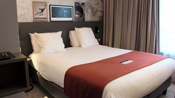 Een hotelkamer met een groot bed, een nachtkastje en een muur met ingelijste foto’s.