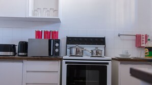 Cozinha com fogão, micro-ondas e cafeteira. Há recipientes vermelhos com os dizeres chá, açúcar e café.