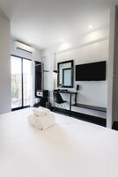 A modern hotel room with a large bed, a desk with a chair, a flat-screen TV mounted on the wall, and an air conditioning unit.