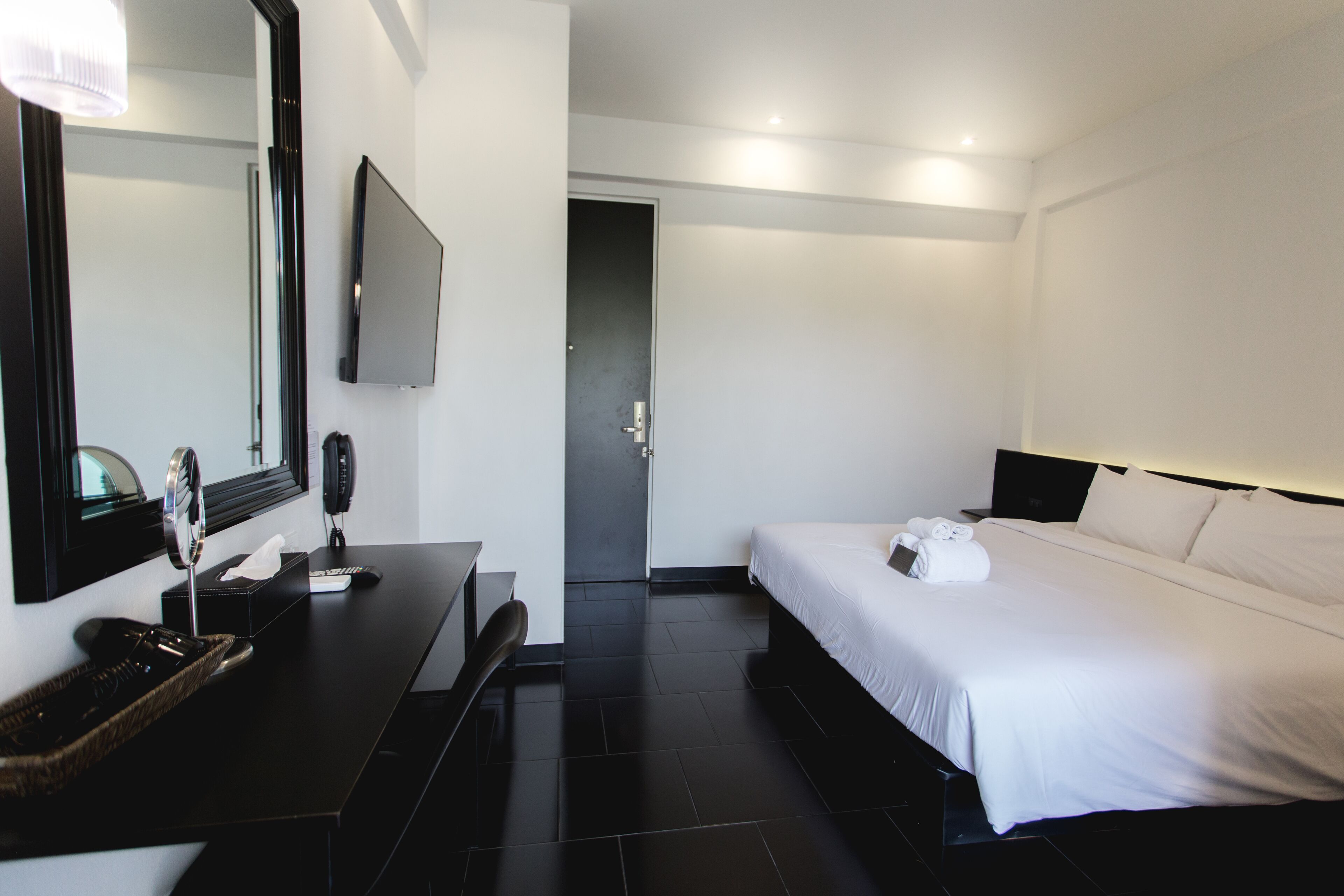A modern hotel room with a large bed, a desk with a computer, a flat-screen TV, and a bathroom door.