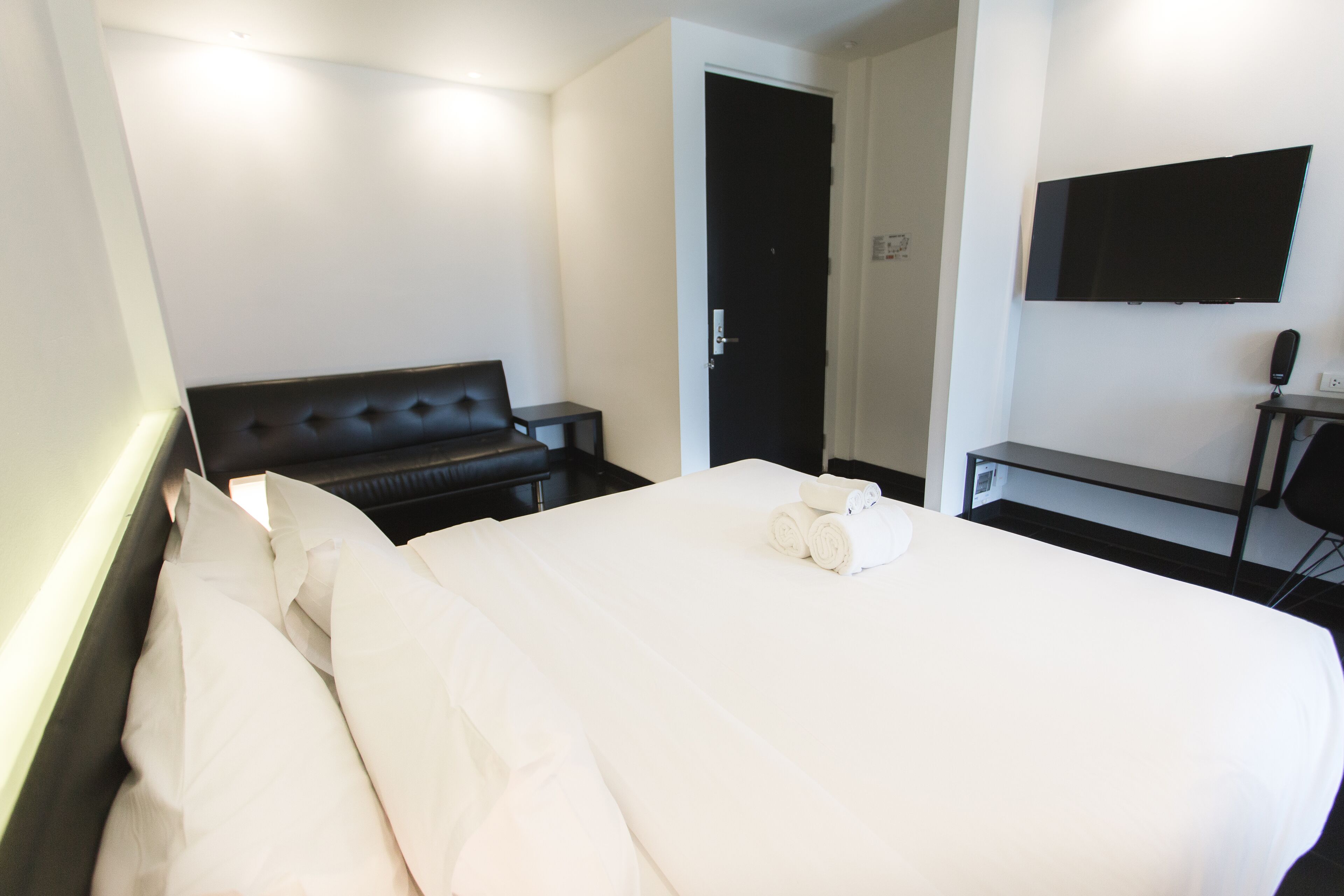 A hotel room with a large bed, a desk, a flat-screen TV, and a door.