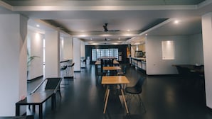 A modern, well-lit office space with multiple tables and chairs, a ceiling fan, and a large window providing natural light. - iSilver Hotel (Chiang Mai)
