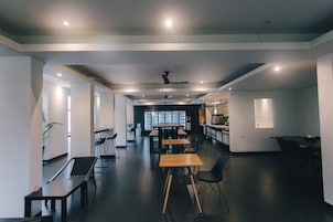 A modern, well-lit office space with multiple tables and chairs, a ceiling fan, and a large window providing natural light.