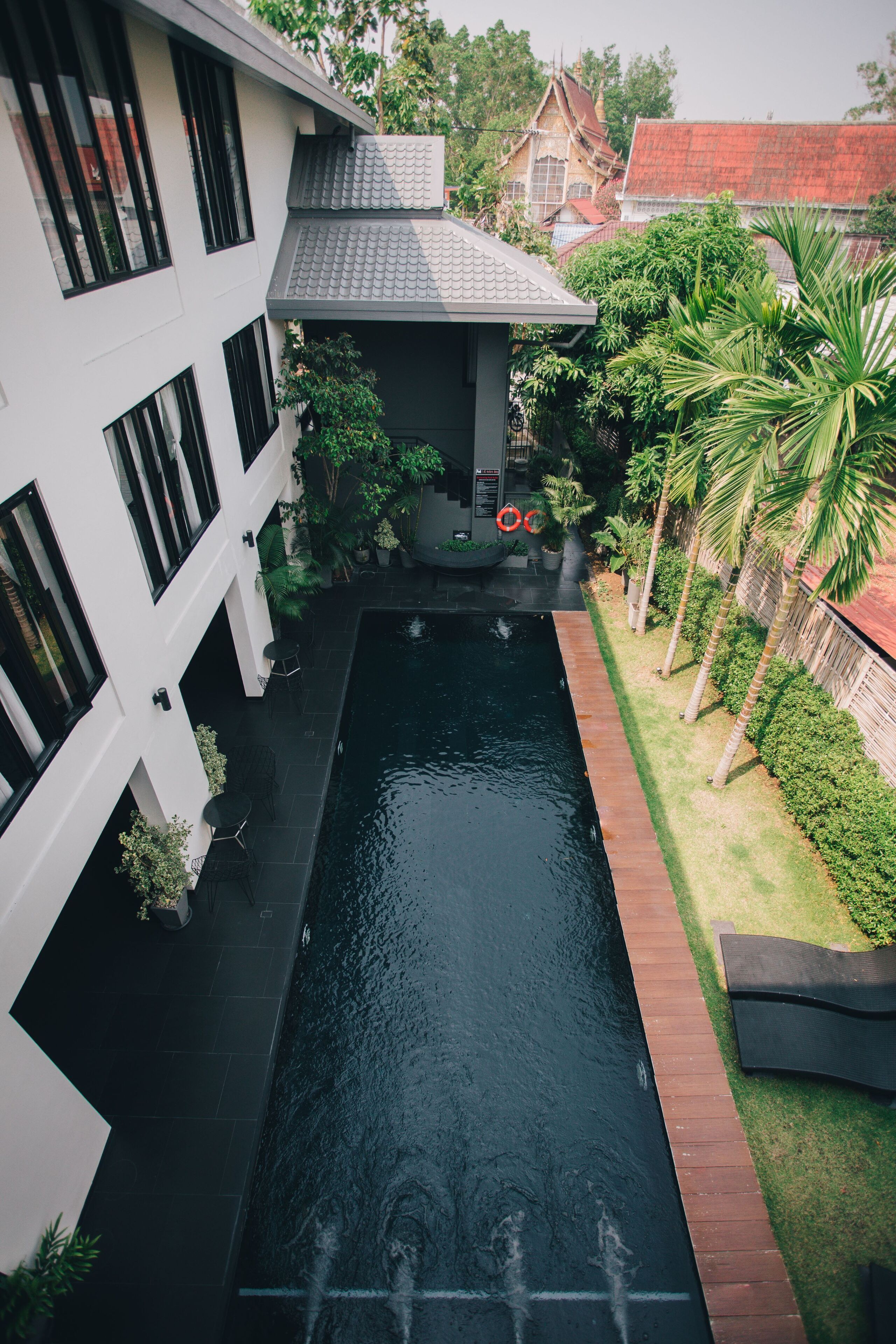Un edificio moderno con piscina, mobiliario exterior y abundante vegetación.