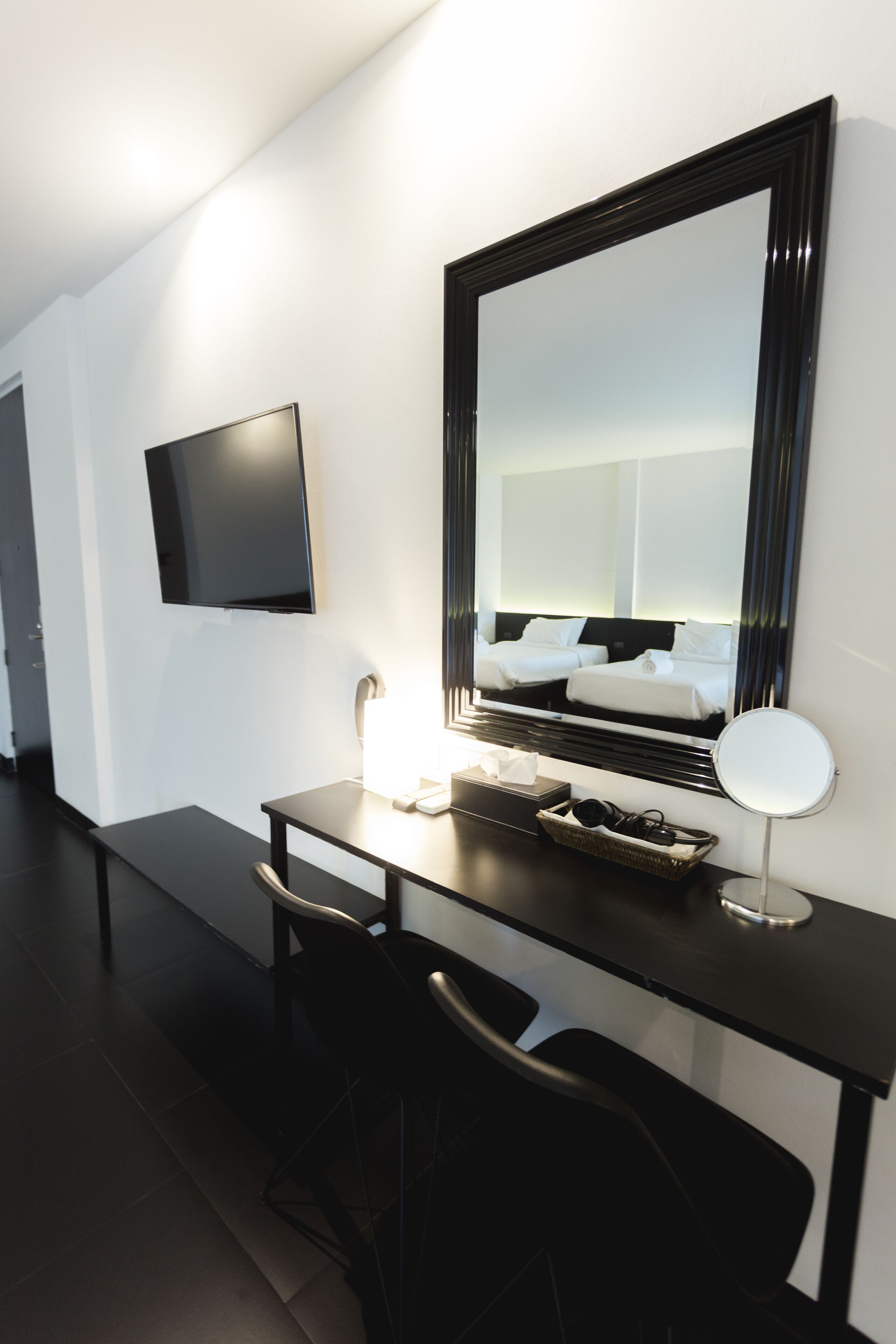 Une chambre d’hôtel moderne équipée d’un grand miroir, d’un téléviseur à écran plat, d’un bureau et d’une chaise.