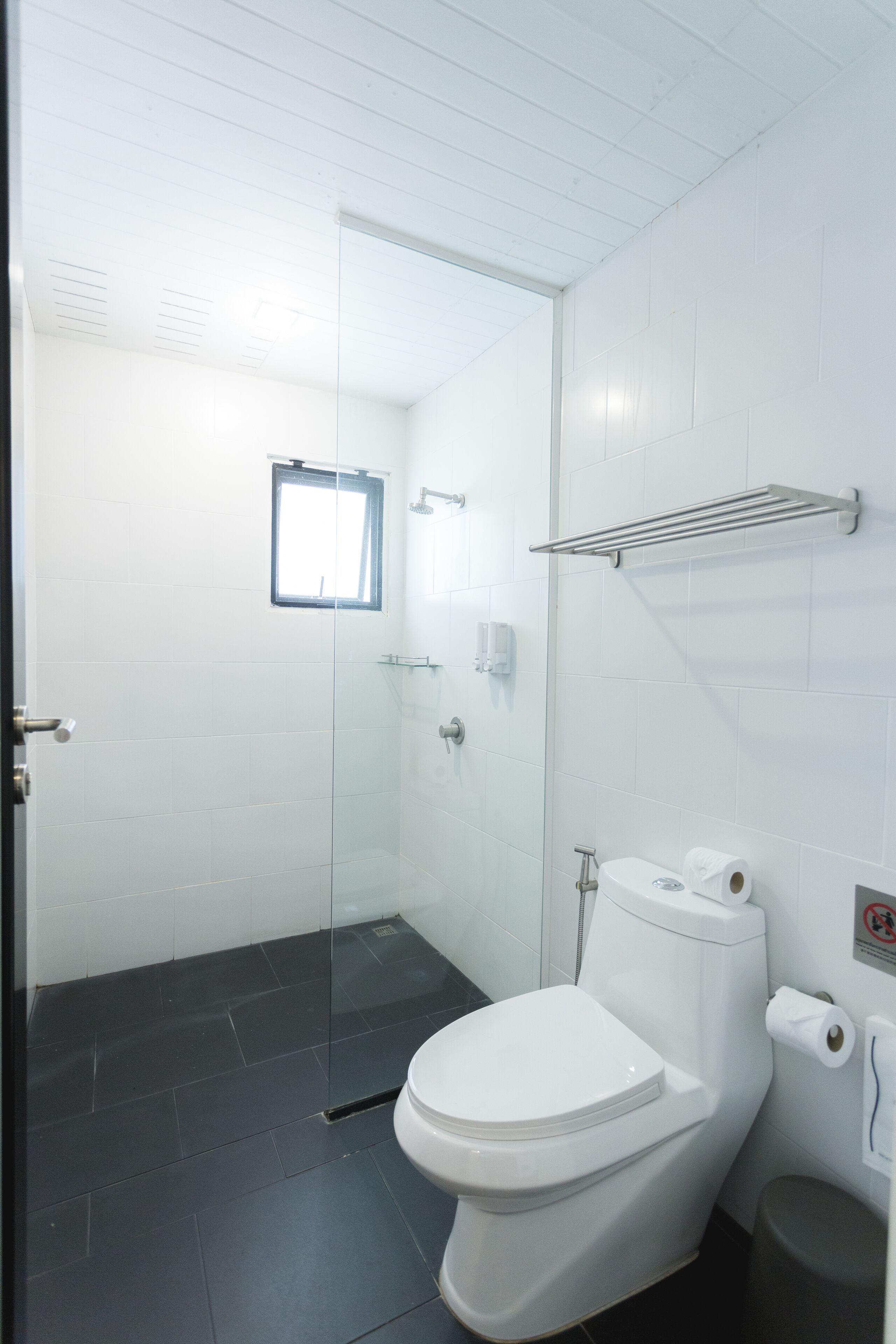 A modern bathroom with a glass shower enclosure, a white toilet, and a small window.