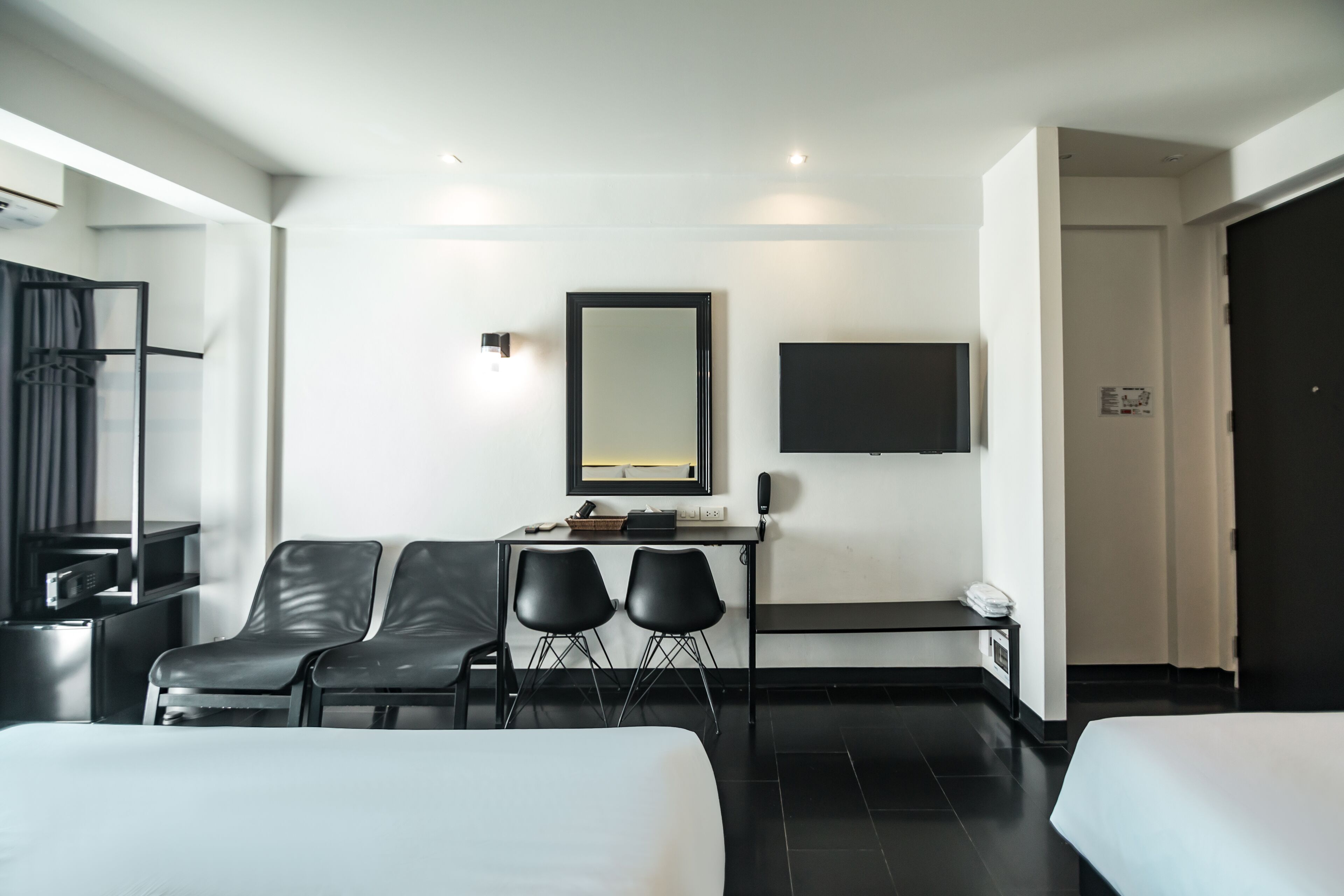 Una habitación de hotel moderna con una cama, un escritorio con dos sillas, un televisor de pantalla plana y un espejo grande.