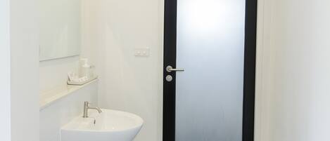 A modern bathroom with a white sink, mirror, and black door.