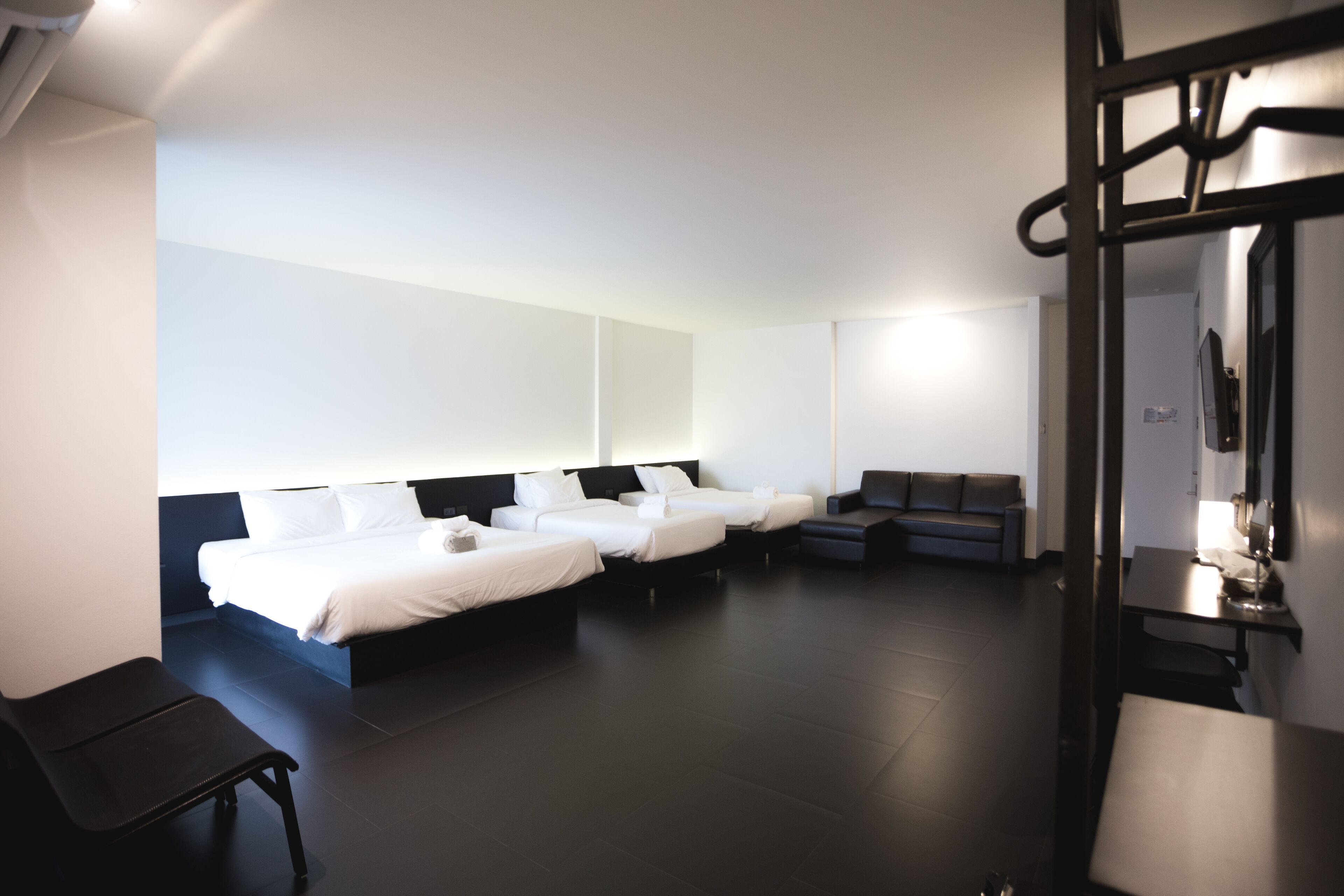 A modern hotel room with three beds, a sofa, and a desk.
